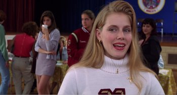 Movie still from “Drop Dead Gorgeous” (1999), directed by Michael Patrick Jann – A woman in a white sweater smiles for the camera; Close Up shot, Over the shoulder angle