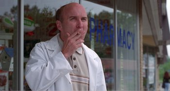 Movie still from “Drop Dead Gorgeous” (1999), directed by Michael Patrick Jann – A man in a white lab coat standing in front of a pharmacy; Medium shot, Low angle