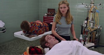 Movie still from “Drop Dead Gorgeous” (1999), directed by Michael Patrick Jann – A woman standing next to a man laying on a bed; Medium shot, Over the shoulder angle