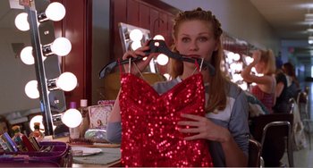Movie still from “Drop Dead Gorgeous” (1999), directed by Michael Patrick Jann – A woman holding a red dress in front of a mirror; Medium shot, High angle