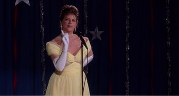 Movie still from “Drop Dead Gorgeous” (1999), directed by Michael Patrick Jann – A woman in a yellow dress holding a microphone; Medium shot, Over the shoulder angle
