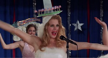 Movie still from “Drop Dead Gorgeous” (1999), directed by Michael Patrick Jann – A woman wearing a white dress and a hat on top of her head; Medium shot, Low angle