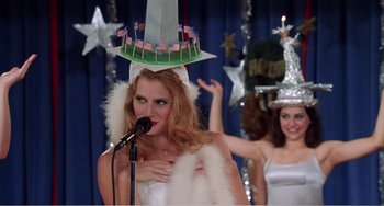 Movie still from “Drop Dead Gorgeous” (1999), directed by Michael Patrick Jann – A woman wearing a hat with a sword on top of her head; Medium shot, Low angle