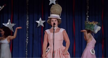 Movie still from “Drop Dead Gorgeous” (1999), directed by Michael Patrick Jann – A woman wearing a pink dress and a top hat on a stage; Medium shot, Low angle