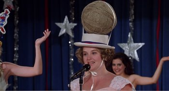 Movie still from “Drop Dead Gorgeous” (1999), directed by Michael Patrick Jann – A woman wearing a top hat with a ball of yarn on top of her head; Medium shot, Low angle