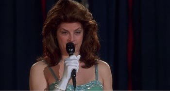 Movie still from “Drop Dead Gorgeous” (1999), directed by Michael Patrick Jann – A woman in a green dress is holding a microphone; Close Up shot, Low angle