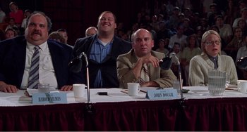 Movie still from “Drop Dead Gorgeous” (1999), directed by Michael Patrick Jann – Two men sitting at a table with microphones in front of them; Medium shot, Low angle