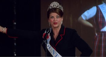 Movie still from “Drop Dead Gorgeous” (1999), directed by Michael Patrick Jann – A woman wearing a tiara standing in front of a microphone; Medium shot, Low angle