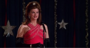 Movie still from “Drop Dead Gorgeous” (1999), directed by Michael Patrick Jann – A woman in a red dress standing in front of a microphone; Medium shot, High angle