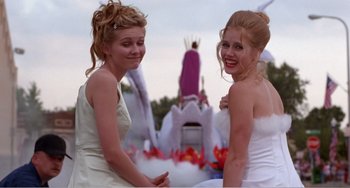 Movie still from “Drop Dead Gorgeous” (1999), directed by Michael Patrick Jann – Two young women are posing for a picture in front of a statue; Medium shot, Low angle