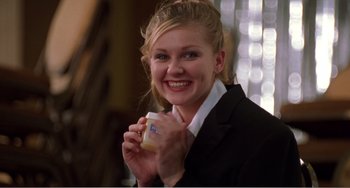 Movie still from “Drop Dead Gorgeous” (1999), directed by Michael Patrick Jann – A woman in a black suit holding a cup of coffee; Medium shot, Low angle