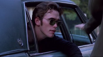 Movie still from “Drugstore Cowboy” (1989), directed by Gus Van Sant – A man sitting in the driver's seat of a car wearing sunglasses; Close Up shot, Over the shoulder angle