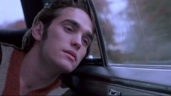 Movie still from “Drugstore Cowboy” (1989), directed by Gus Van Sant – A man sitting in the passenger seat of a car looking out the window; Close Up shot, Low angle
