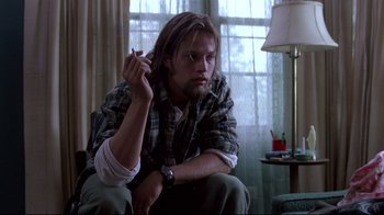 Movie still from “Drugstore Cowboy” (1989), directed by Gus Van Sant – A man sitting in a chair with a cigarette in his mouth; Medium shot, Low angle