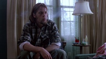 Movie still from “Drugstore Cowboy” (1989), directed by Gus Van Sant – A man sitting on a chair in a living room; Medium shot, Low angle