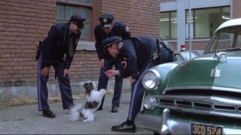Movie still from “Drugstore Cowboy” (1989), directed by Gus Van Sant – A group of police officers standing next to an old car; Wide shot, Over the shoulder angle