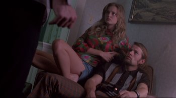 Movie still from “Drugstore Cowboy” (1989), directed by Gus Van Sant – A man and a woman sitting on top of a couch next to another man; Medium shot, Over the shoulder angle