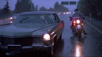 Movie still from “Drugstore Cowboy” (1989), directed by Gus Van Sant – A car and a motorcycle on a wet road; Wide shot, Low angle