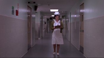 Movie still from “Drugstore Cowboy” (1989), directed by Gus Van Sant – A woman standing in a hallway holding a clipboard; Wide shot, Low angle