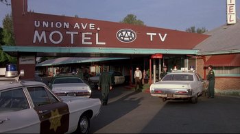 Movie still from “Drugstore Cowboy” (1989), directed by Gus Van Sant – Two men walk down the street in front of a motel; Wide shot, Low angle