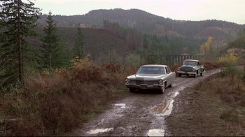 Movie still from “Drugstore Cowboy” (1989), directed by Gus Van Sant – A couple of cars parked on top of a dirt road; Extreme Wide shot, High angle