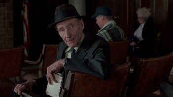 Movie still from “Drugstore Cowboy” (1989), directed by Gus Van Sant – An older man sitting in a chair with a hat on; Medium shot, Over the shoulder angle