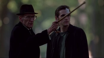 Movie still from “Drugstore Cowboy” (1989), directed by Gus Van Sant – An older man and a younger man are holding a bow and arrow; Medium shot, Over the shoulder angle