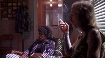Movie still from “Drugstore Cowboy” (1989), directed by Gus Van Sant – A man smoking a cigarette while sitting next to another man; Medium shot, Over the shoulder angle