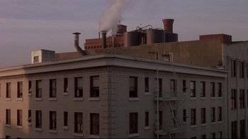 Movie still from “Drugstore Cowboy” (1989), directed by Gus Van Sant – Smoke billows out of a factory on top of a building; Extreme Wide shot, Low angle