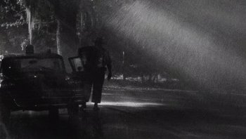 Movie still from “The Paperboy” (2012), directed by Lee Daniels – A person standing in the rain near a bench; Wide shot, Low angle