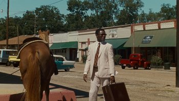 Movie still from “The Paperboy” (2012), directed by Lee Daniels – A man in a white suit walking down the street with a horse; Wide shot, Over the shoulder angle