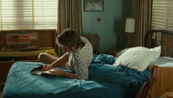 Movie still from “The Paperboy” (2012), directed by Lee Daniels – A woman sitting on a bed writing on a book; Medium shot, Over the shoulder angle