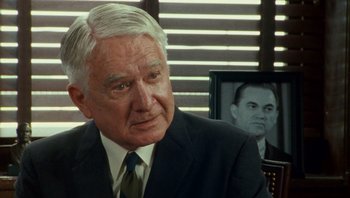 Movie still from “The Paperboy” (2012), directed by Lee Daniels – An older man wearing a suit and tie in front of a picture of himself; Close Up shot, Over the shoulder angle