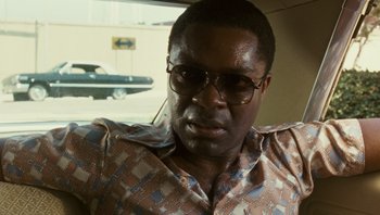 Movie still from “The Paperboy” (2012), directed by Lee Daniels – A person wearing glasses with a car in the background; Close Up shot, Over the shoulder angle