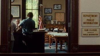 Movie still from “The Paperboy” (2012), directed by Lee Daniels – A man standing in front of a desk in a room; Wide shot, Over the shoulder angle