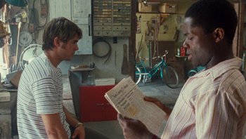 Movie still from “The Paperboy” (2012), directed by Lee Daniels – A man reading a newspaper while a boy watches; Medium shot, Over the shoulder angle