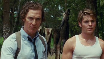 Movie still from “The Paperboy” (2012), directed by Lee Daniels – A man standing next to another man in a forest; Medium shot, Low angle