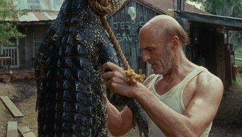 Movie still from “The Paperboy” (2012), directed by Lee Daniels – A bald man is tying a rope to a large alligator; Medium shot, Low angle