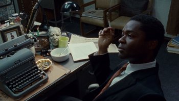 Movie still from “The Paperboy” (2012), directed by Lee Daniels – A man sitting at a table in a room; Medium shot, High angle