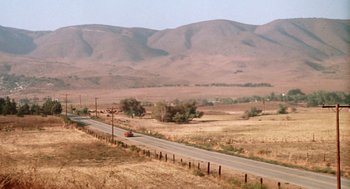 Movie still from “Duel” (1971), directed by Steven Spielberg – An orange truck driving down a road in the middle of a desert; Extreme Wide shot, High angle