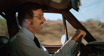 Movie still from “Duel” (1971), directed by Steven Spielberg – A man driving a car on a road; Close Up shot, Low angle