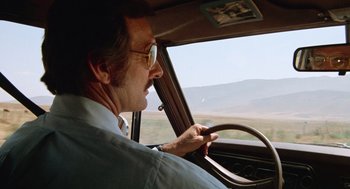 Movie still from “Duel” (1971), directed by Steven Spielberg – An older man driving a car in the middle of the day; Medium shot, Low angle