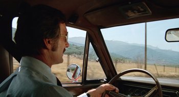 Movie still from “Duel” (1971), directed by Steven Spielberg – A man driving a car on a road; Medium shot, Low angle