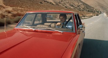 Movie still from “Duel” (1971), directed by Steven Spielberg – A man driving a red car on the side of the road; Wide shot, Low angle