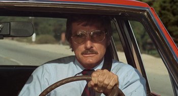 Movie still from “Duel” (1971), directed by Steven Spielberg – A man driving a car wearing a tie and sunglasses; Close Up shot, Low angle
