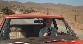 Movie still from “Duel” (1971), directed by Steven Spielberg – A man driving a red car on the side of the road; Wide shot, Low angle