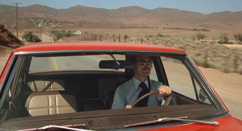 Movie still from “Duel” (1971), directed by Steven Spielberg – A man driving a red car on a road; Wide shot, Low angle