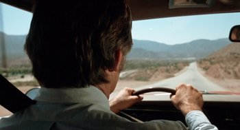 Movie still from “Duel” (1971), directed by Steven Spielberg – A man driving a car on a road with mountains in the background; Wide shot, Over the shoulder angle