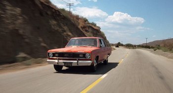 Movie still from “Duel” (1971), directed by Steven Spielberg – An orange car driving down a road near a hill; Wide shot, Low angle