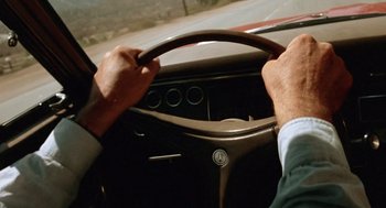Movie still from “Duel” (1971), directed by Steven Spielberg – A man driving a car on the street; Close Up shot, High angle